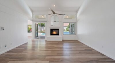 A spacious modern living room with hardwood flooring, white walls, and a centered fireplace beneath an arched alcove.