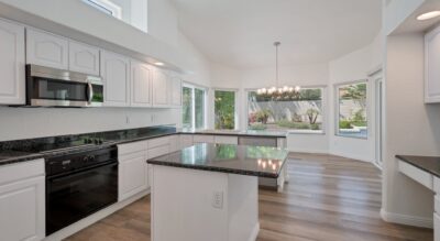 Modern kitchen with white cabinetry, black granite countertops, stainless steel appliances, and a view of the garden through large windows.